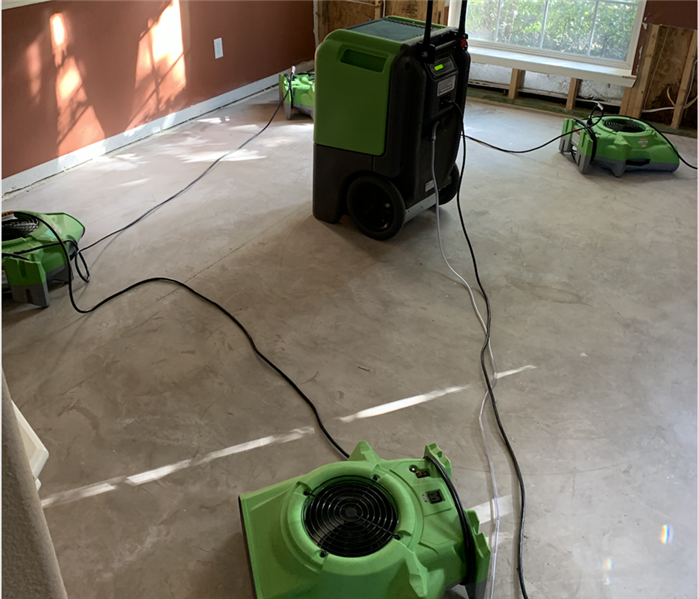 Air movers and dehumidifier set up on the floor of an empty bedroom.