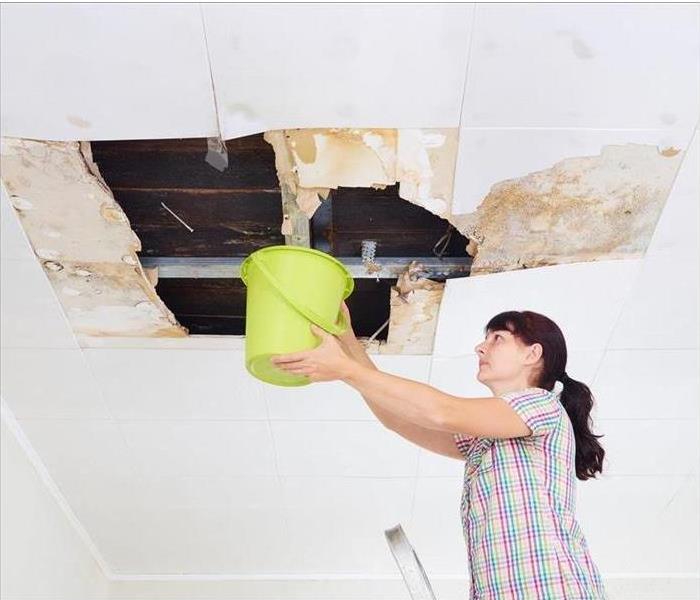 Image of a person holding a bucket under a water leak from the ceiling. 