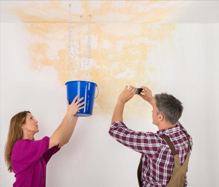 Image of 2 persons dealing with a leak from the ceiling of a building. 